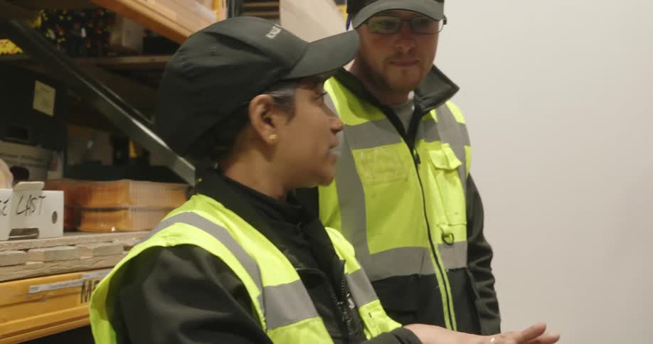 Two professionals wearing safety vests inspect shelves in a warehouse environment