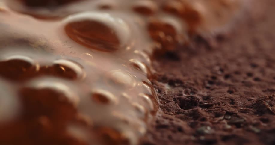 A macro closeup reveals bubbling liquid spreading over a porous chocolatey surface highlighting rich texture and movement