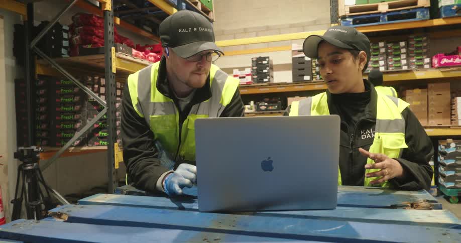 Two supermarket employees a man and a woman sitting at a table in front of a laptop talking
