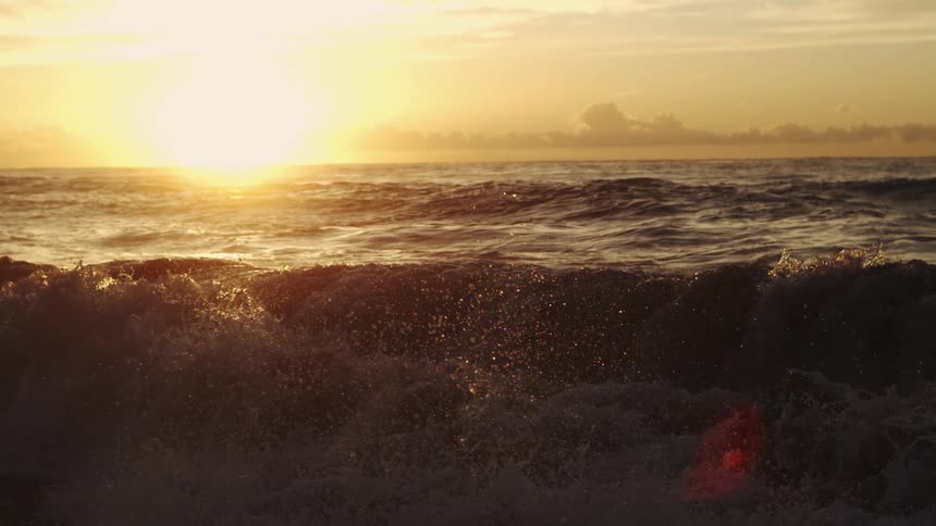 Birds fly over the waves flowing toward shore under a red sky during sunrise