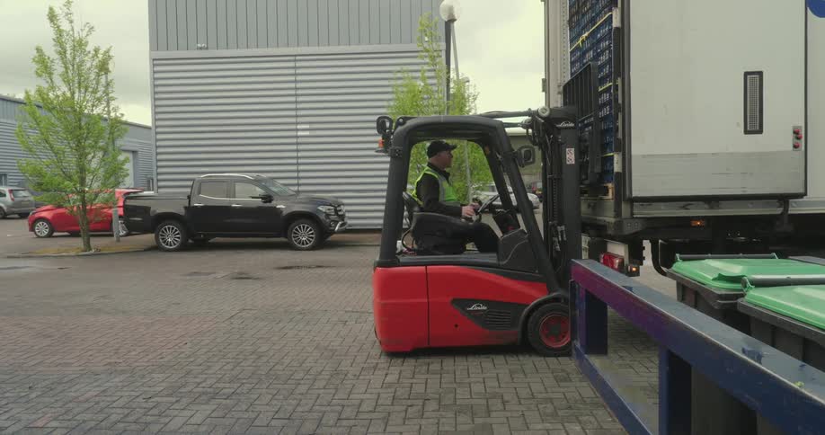 A forklift operator is loading or unloading goods from a trailer truck in an industrial parking lot