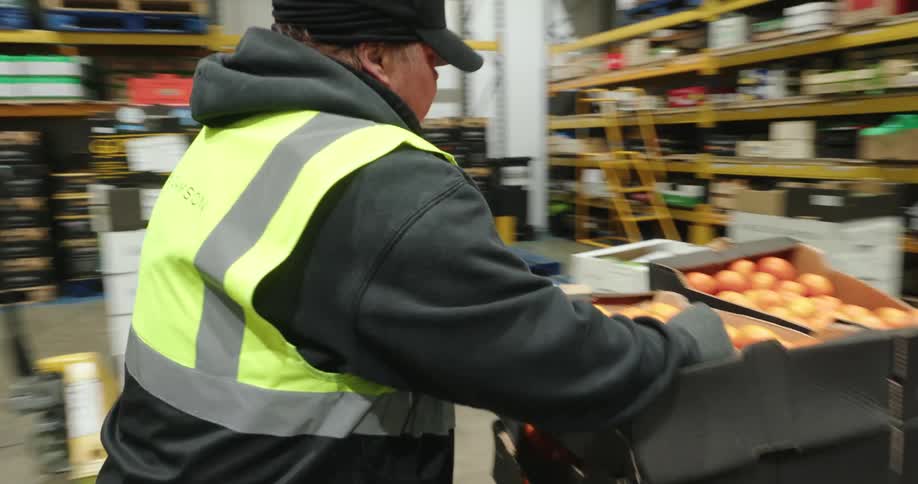 Warehouse worker pushing crates of oranges across warehouse stock room