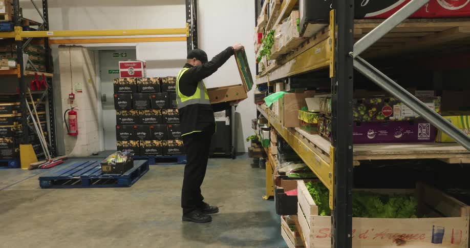 A male worker putting boxes on the shelve in a warehouse at night
