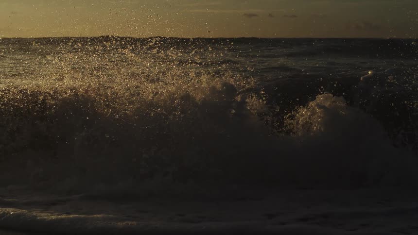 Waves form and splash against the seashore at dusk