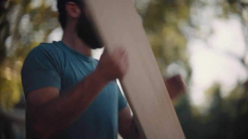 Man picks up a wooden plank and places it on a workbench