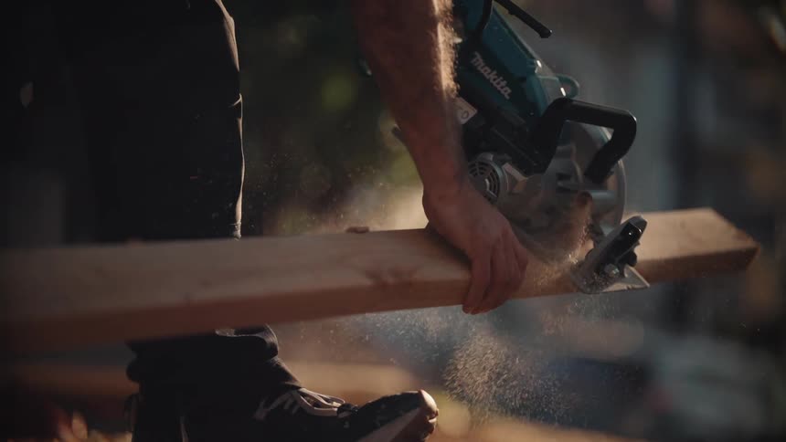 A man outdoors holding a piece of wood and cutting it with an electric saw