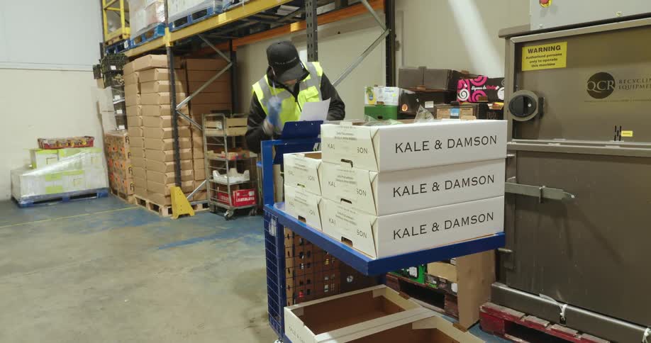A man labels boxes on a trolley and pushes the trolley into another room shortly after