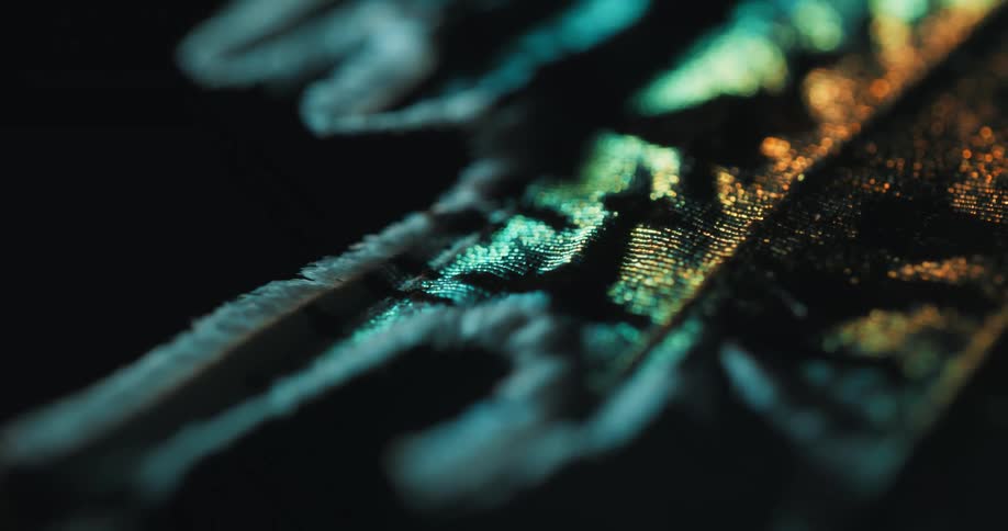 An extreme closeup of intricately textured shimmering fibers in teal and amber lighting creates a strikingly abstract visual