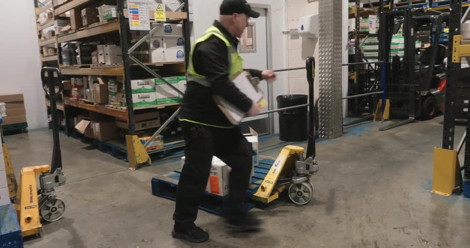 Male warehouse worker moves boxes using a pallet and a hand trolley