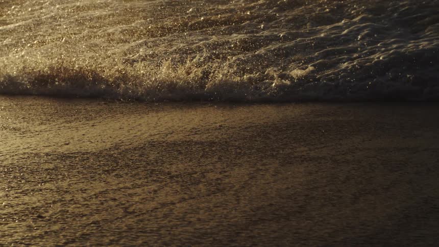 A sea wave breaking on the sand of a beach and making a splash of drops upwards
