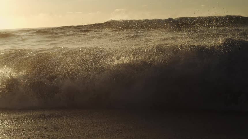 A sea wave breaking on a sandy shore on a morning with an orange sky