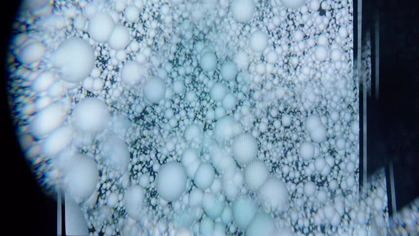 A highly magnified abstract image shows a dense cluster of translucent spheres or bubbles in a surreal scientificlike arrangement