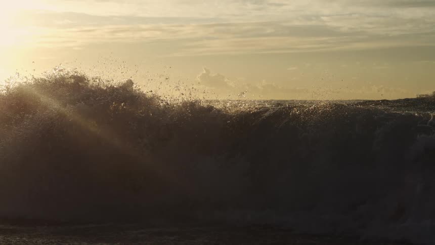 Slow motion of large barrel wave crashing on the shoreline at dawn