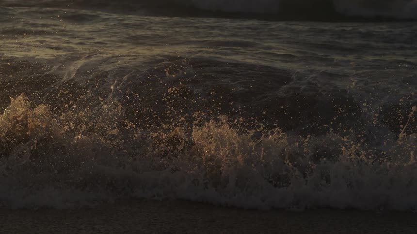 A small sea wave breaking on the shore making a splash of drops upwards