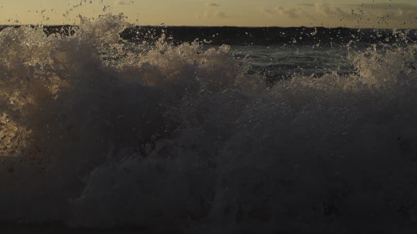 The wave crashes on the sand at sunrise