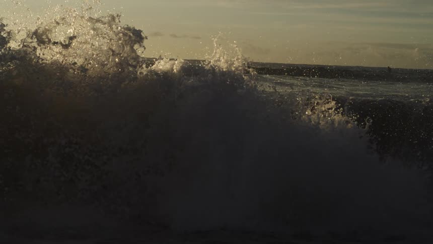 A small wave wave of the sea breaking on the shore making a splash on a morning with the sky partially orange