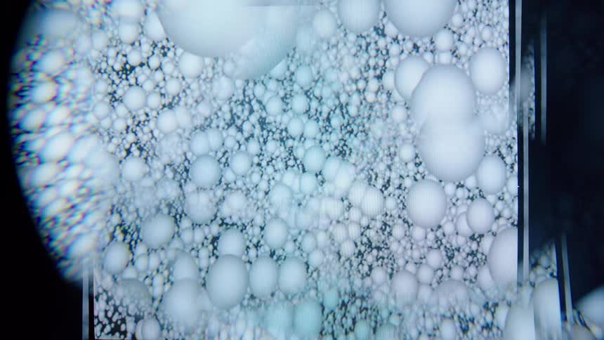 A series of white spheres orbiting inside a transparent glass enclosure appearing to move in a circular or spiral path within the container