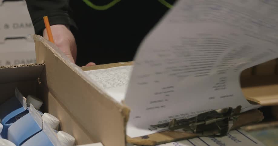 A person writes on a clipboard form likely checking inventory in a warehouse