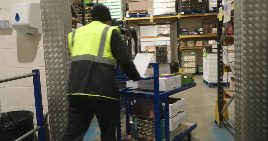 A man in a safety vest and wearing a cap driving a cart through a vegetable distribution warehouse