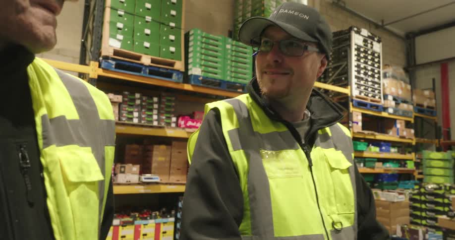 The warehouse workers smile and laugh together while standing in a well stocked industrial warehouse suggesting a lighthearted moment during their shift