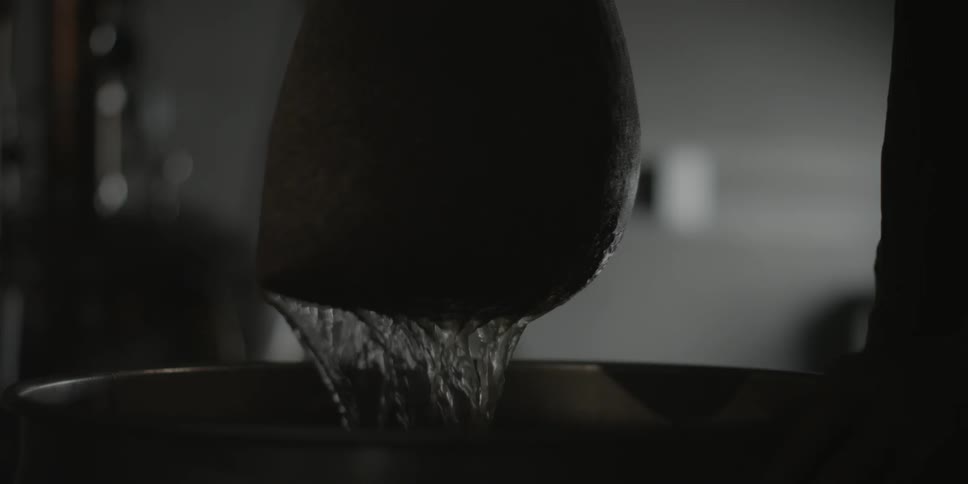 A person lifts a filled bag from a barrel of water