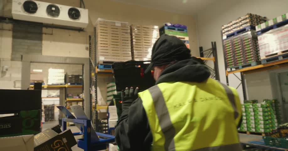 Man pushes a loaded warehouse cart across the room towards a doorway in a warehouse