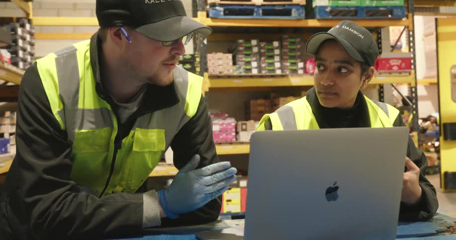 Two coworkers converse in front of a mac on a tabletop