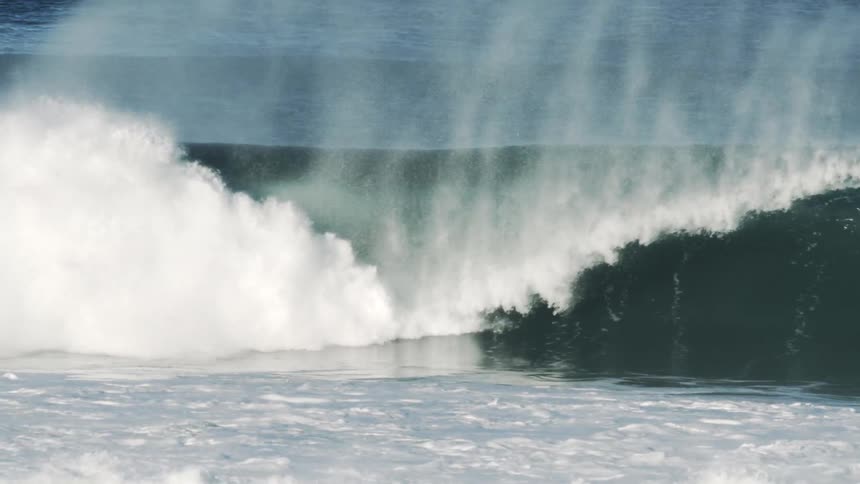 A surfer rides and is covered by an ocean wave during the day
