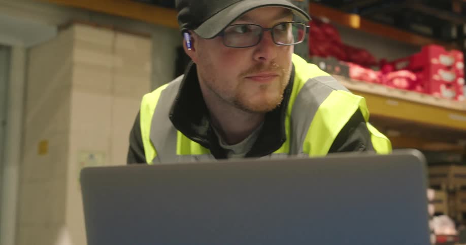 The worker is looking at a laptop while talking with coworkers