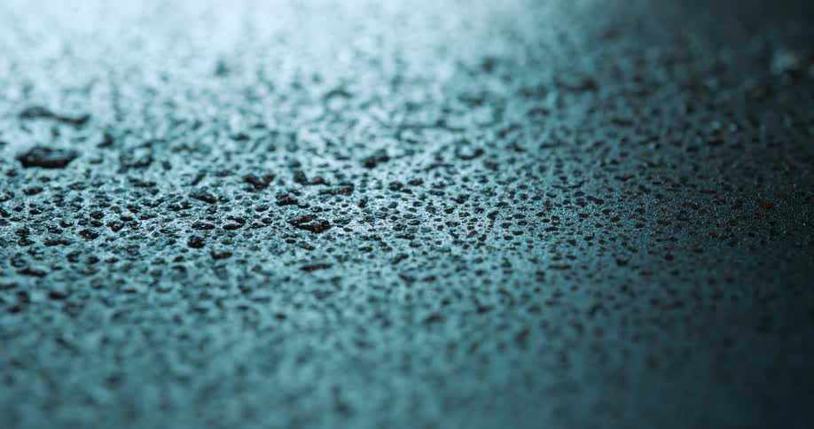 A blue surface with several water droplets and a bright light coming from above