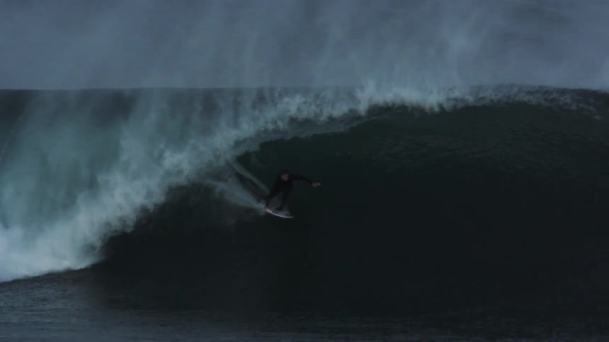 A surfer emerges from the inside of a wave
