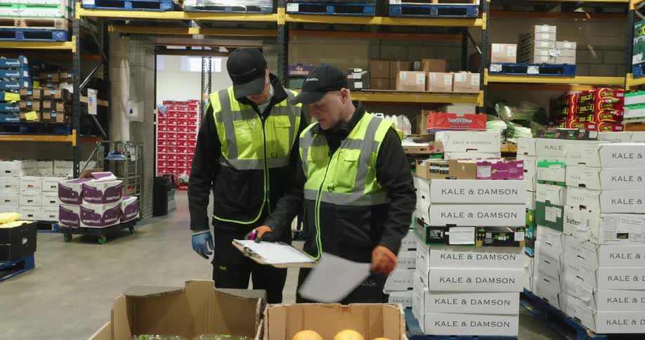 Two men in a warehouse talking and checking a sheet of paper