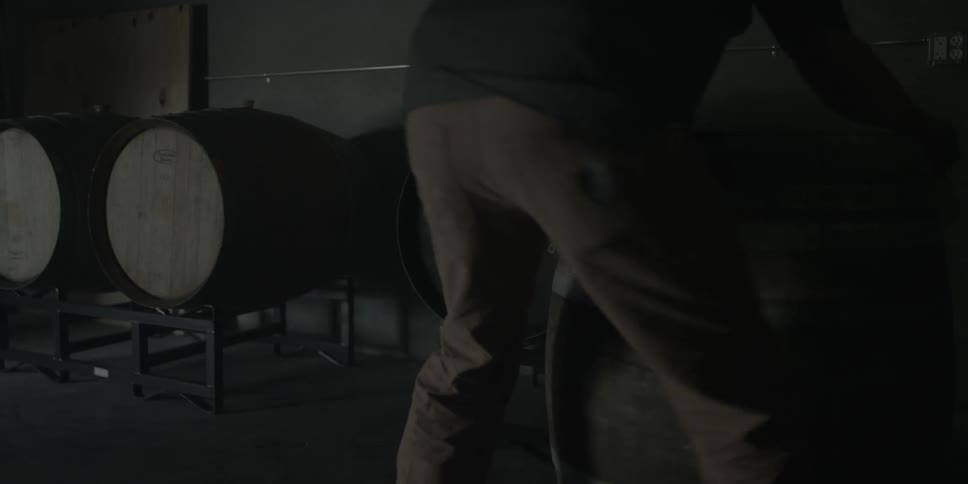 Person rolls a wooden barrel to set it next to two other barrels