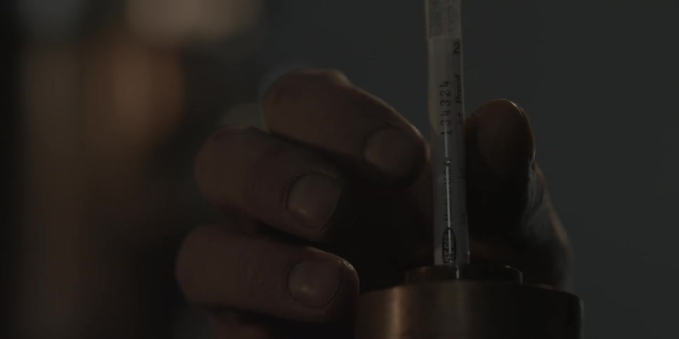 A hand touches a thermometer that is rising from a cylinder