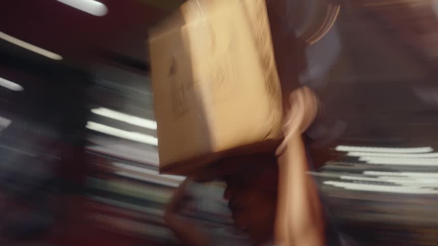 At a chaotic street bazaar in india a man walks by with a large box on his head