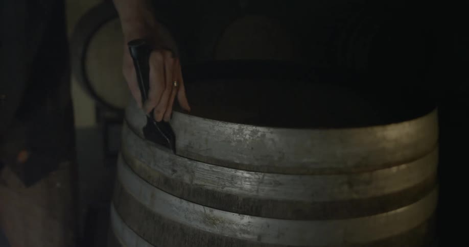 A man tightens the rings on a whiskey barrel