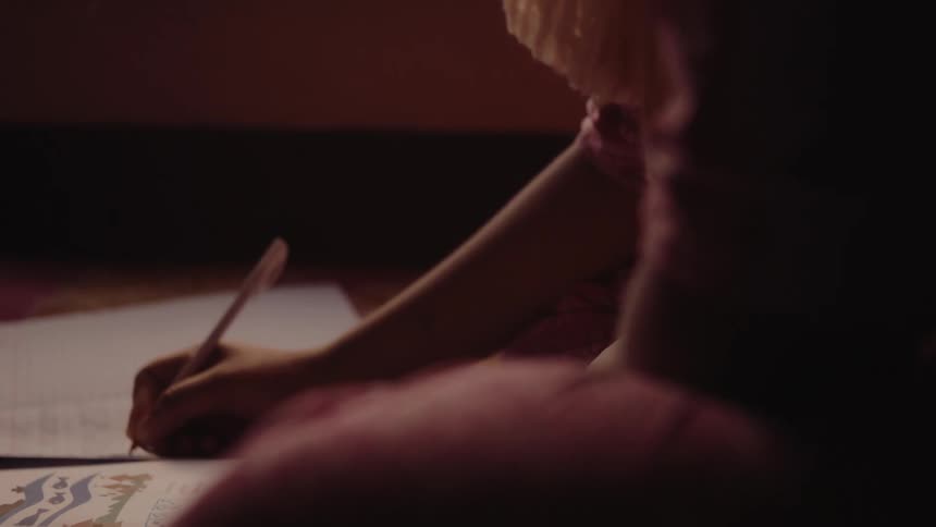 A woman sitting on the floor indoors at midday writing in a notebook with natural light streaming in