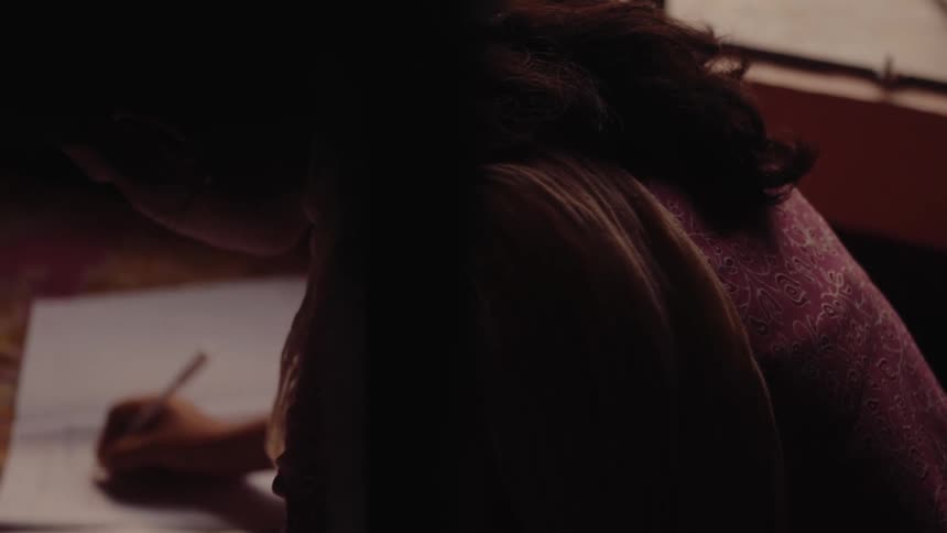A woman sitting on the floor indoors at midday writing in a white notebook