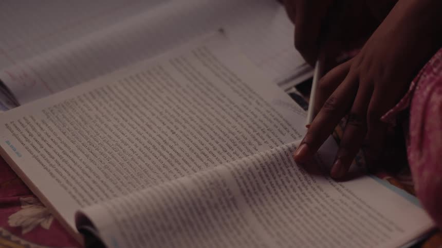 A person is studying with a pencil in hand and a textbook open deeply focused on writing in a notebook