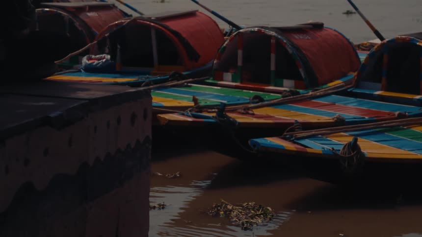 Colorfully painted canoes with little roofs sit in a row on a murky lake