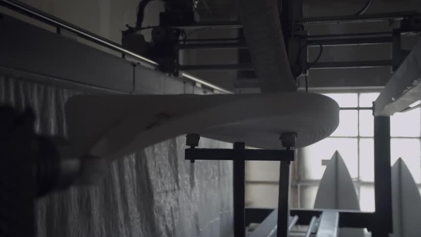 An industrial machine with a brush makes a pass over a surfboard