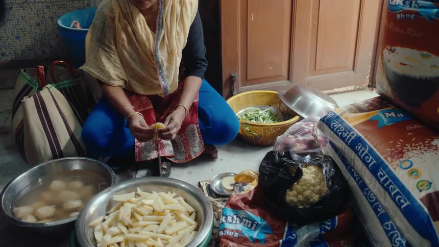 A woman is sitting on the floor while cutting potatoes