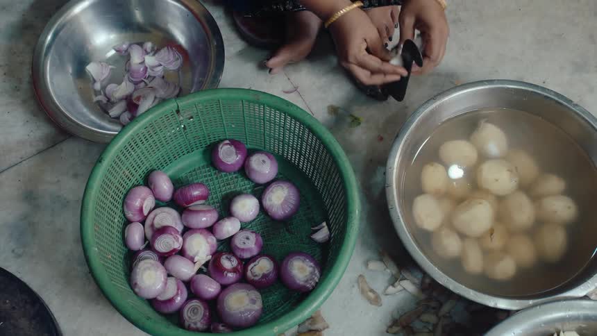 Woman cutting onions on a kitchen tool on the floor beside bowls with onions and potatoes