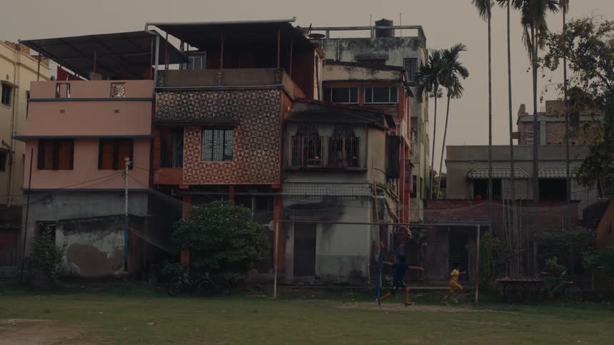 A boy kicks a ball towards the goalpost with another boy trying to catch in the evening