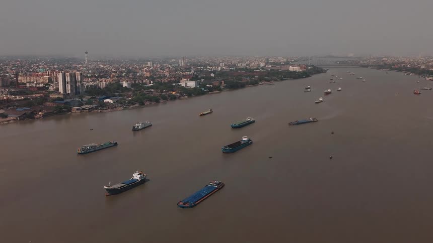 A series of ships are docked in the ocean water with a city skyline visible to the side at midday