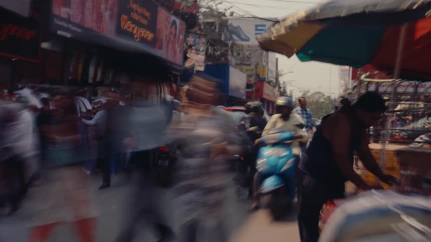 A chaotic indian street with street sales stands people scooters and cars everywhere