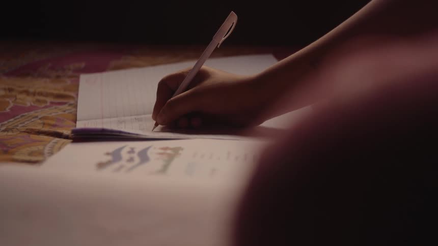 A person writes with a pen on sheets of paper resting on a patterned surface