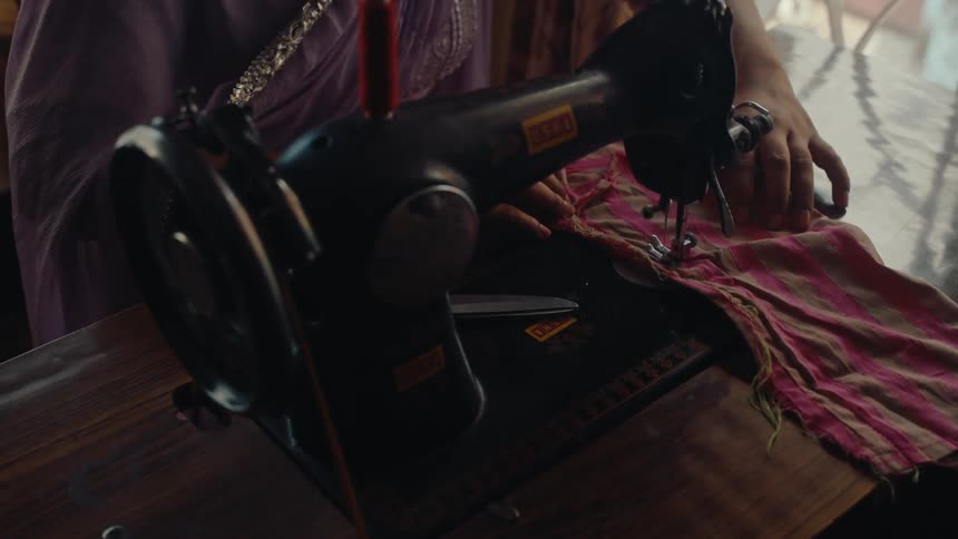 The woman feeds the fabric through the sewing machine