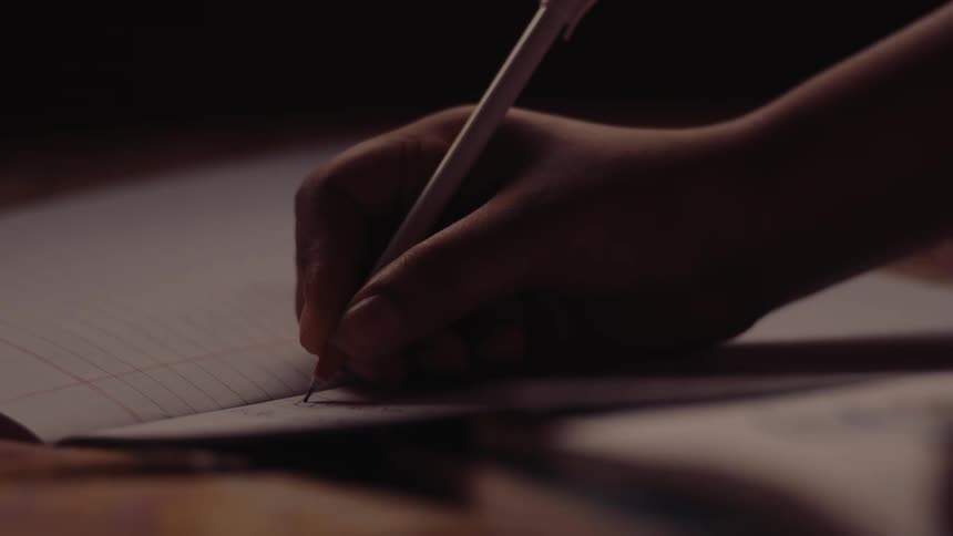 Hand jotting notes a notebook in a dim lit room