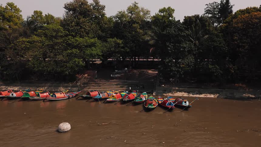 A river with several canoes docked along the riverbank and people standing by the shore